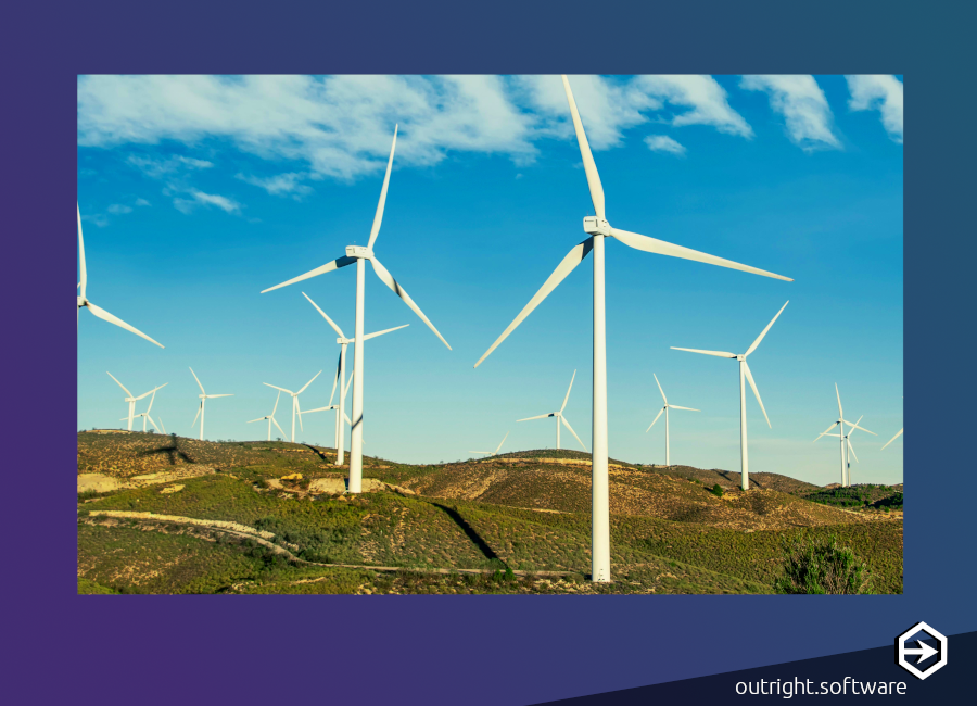 White windmills on the backdrop of a bright blue sky with minimal clouds. They are spread out over an uneven, green landscape. They are used as an alternative to carbon emission emitting coal.